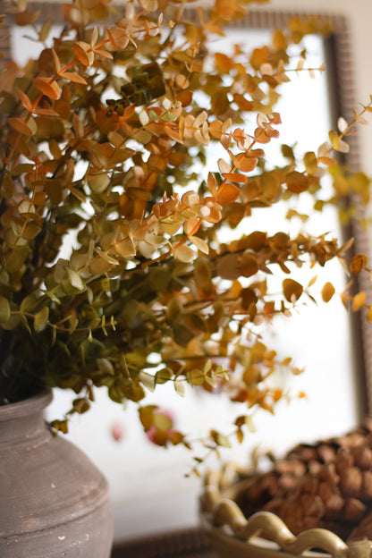 Decorative autumn faux plant with orange and green leaves in a pot, blurred background