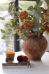 Autumn decorative setup with a vase of autumn berry stems and silver dollar eucalyptus , books, and small items on a surface.