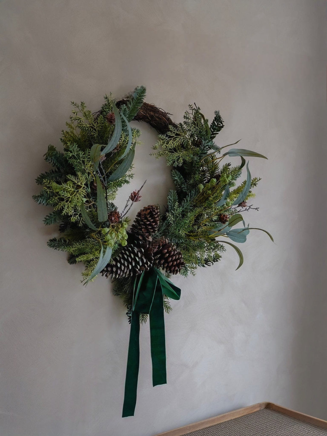Christmas green faux foliage wreath with pinecones and a ribbon on a plain wall