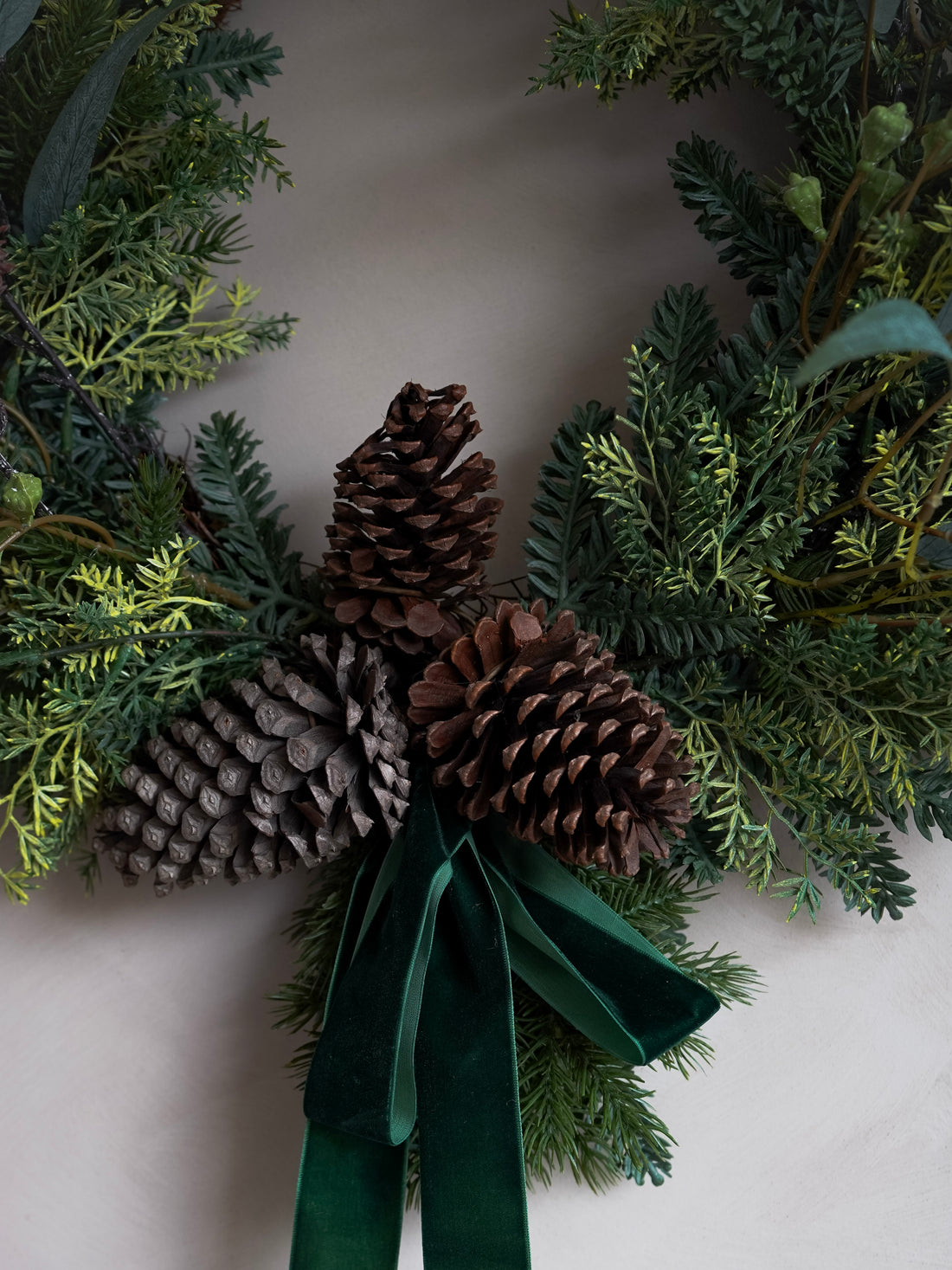 Decorative wreath with pine cones and a green ribbon on a neutral background
