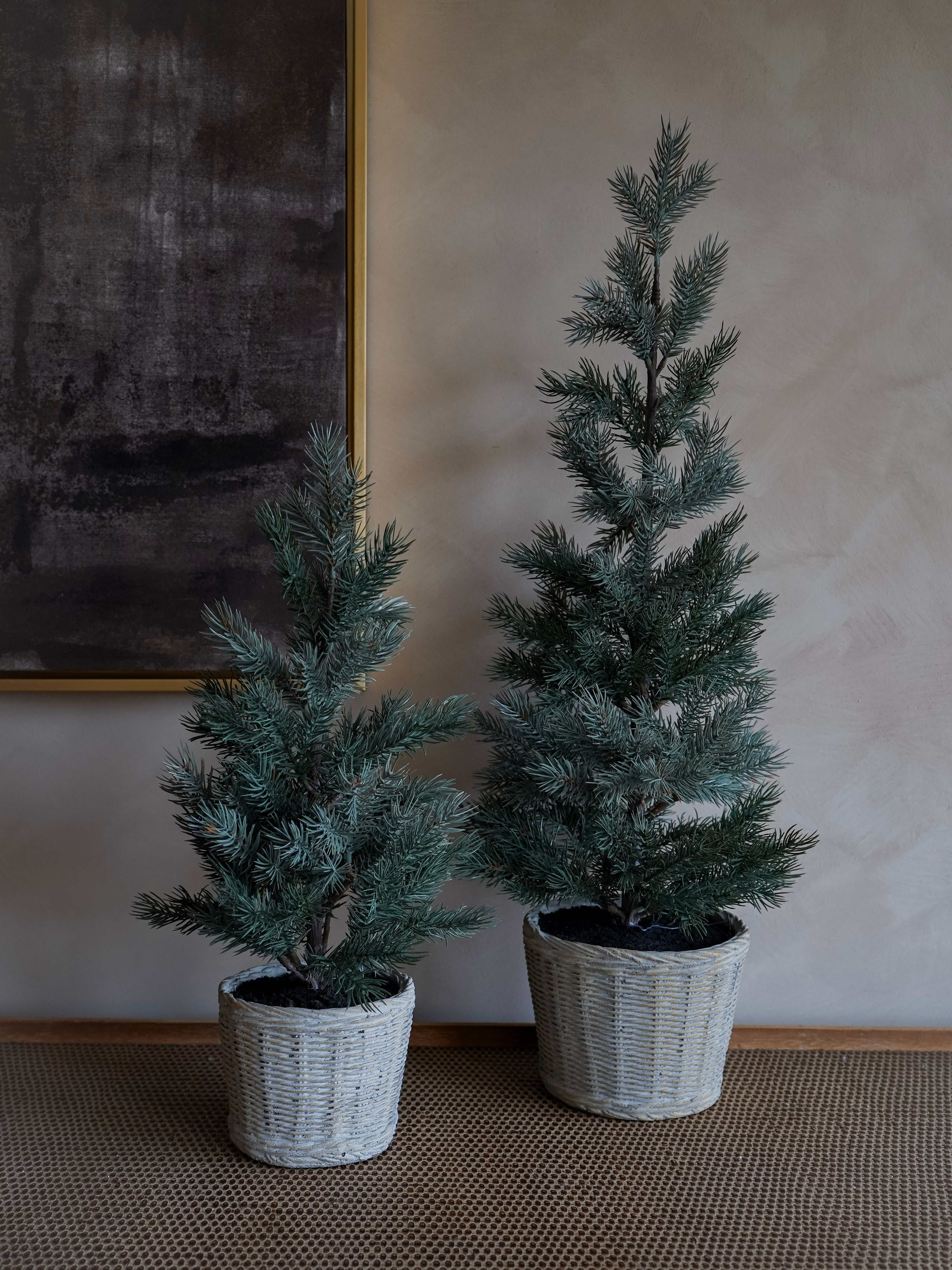 Two potted artificial christmas  trees against a neutral wall.