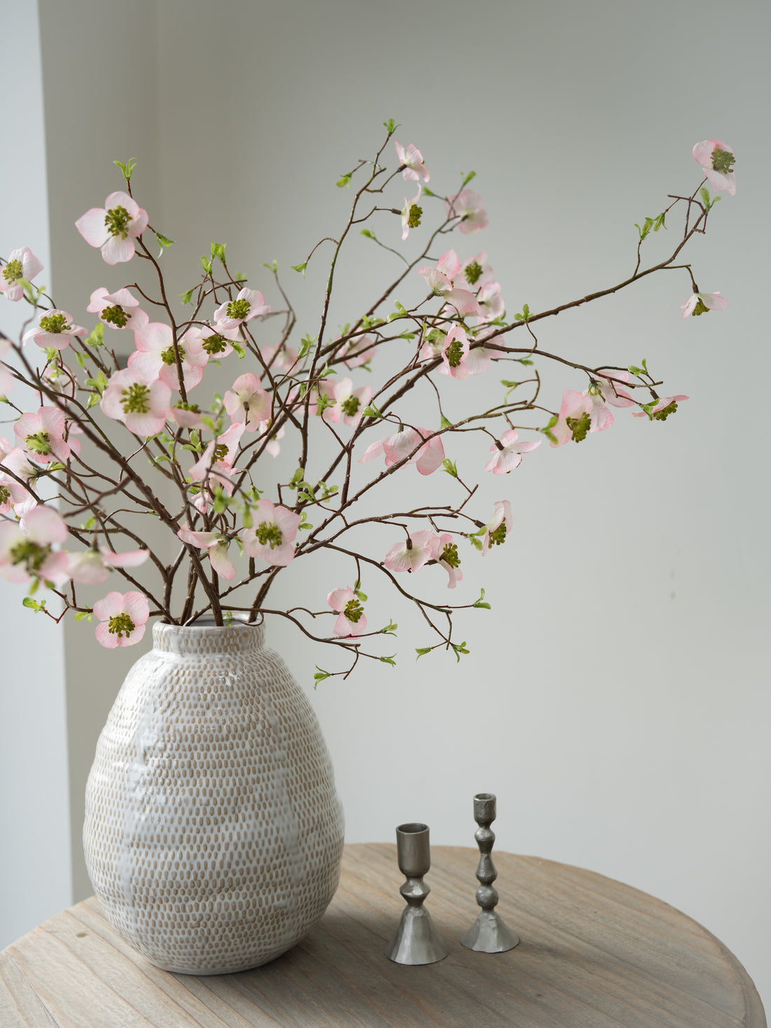 Decorative vase with faux pink dogwood flowers on a wooden table against a plain wall
