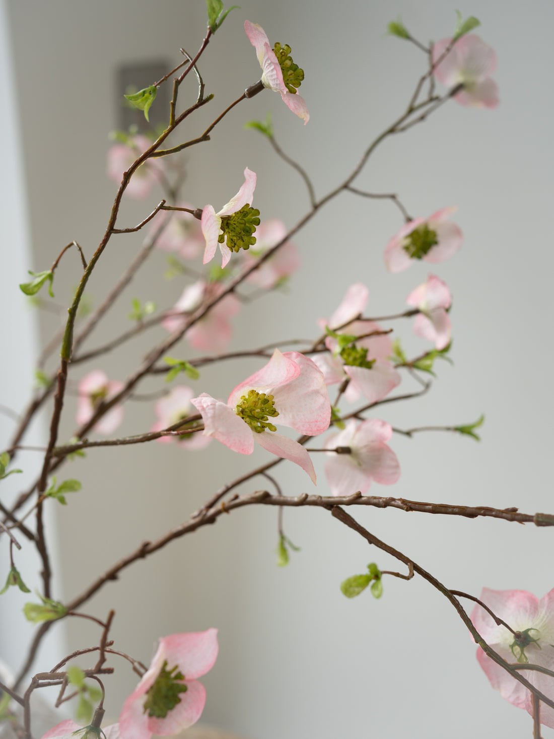 Faux pink dogwood flowers on a branch against a light background