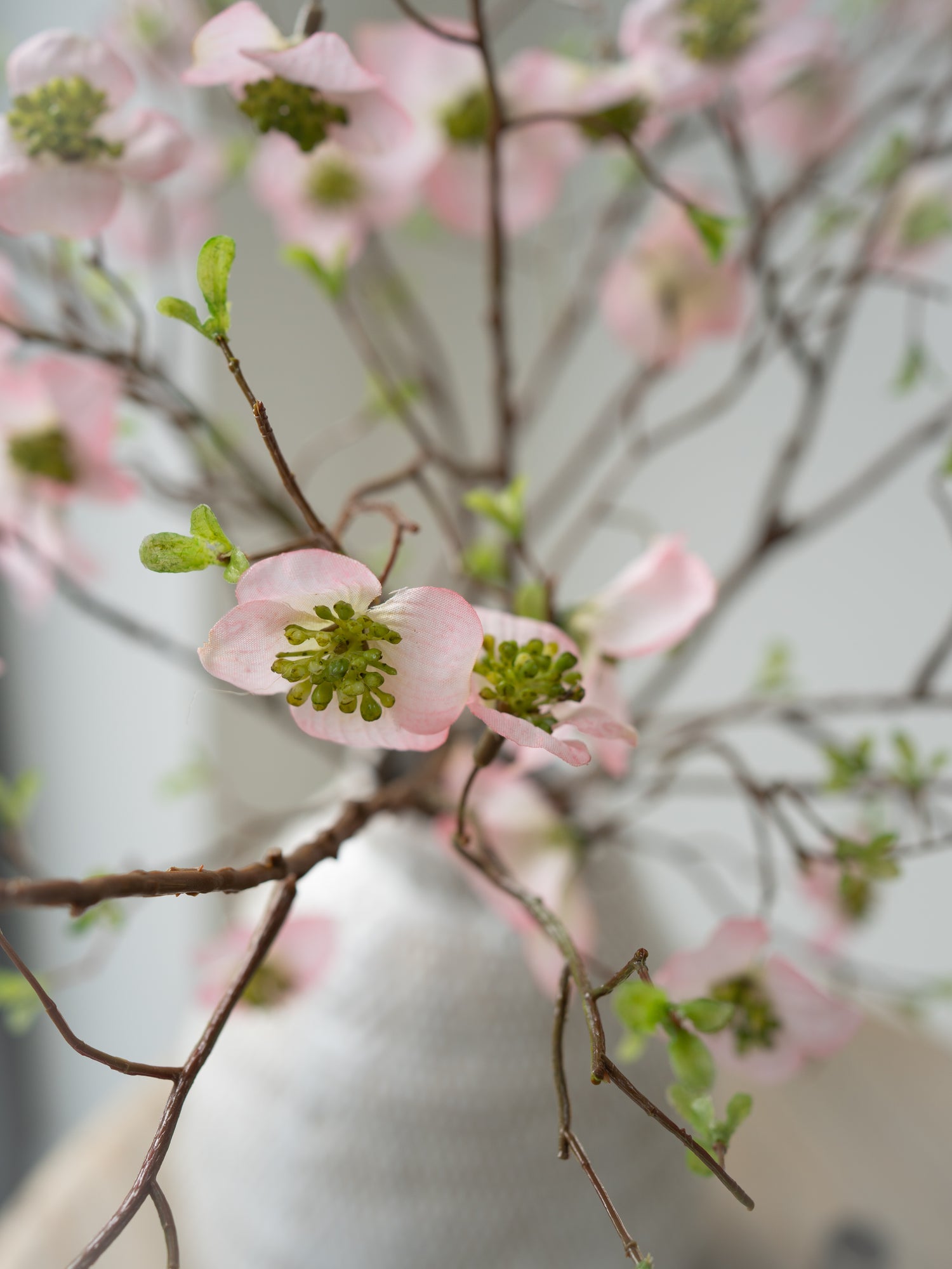 Close-up of faux pink dogwood flowers with a blurred white vase in the background