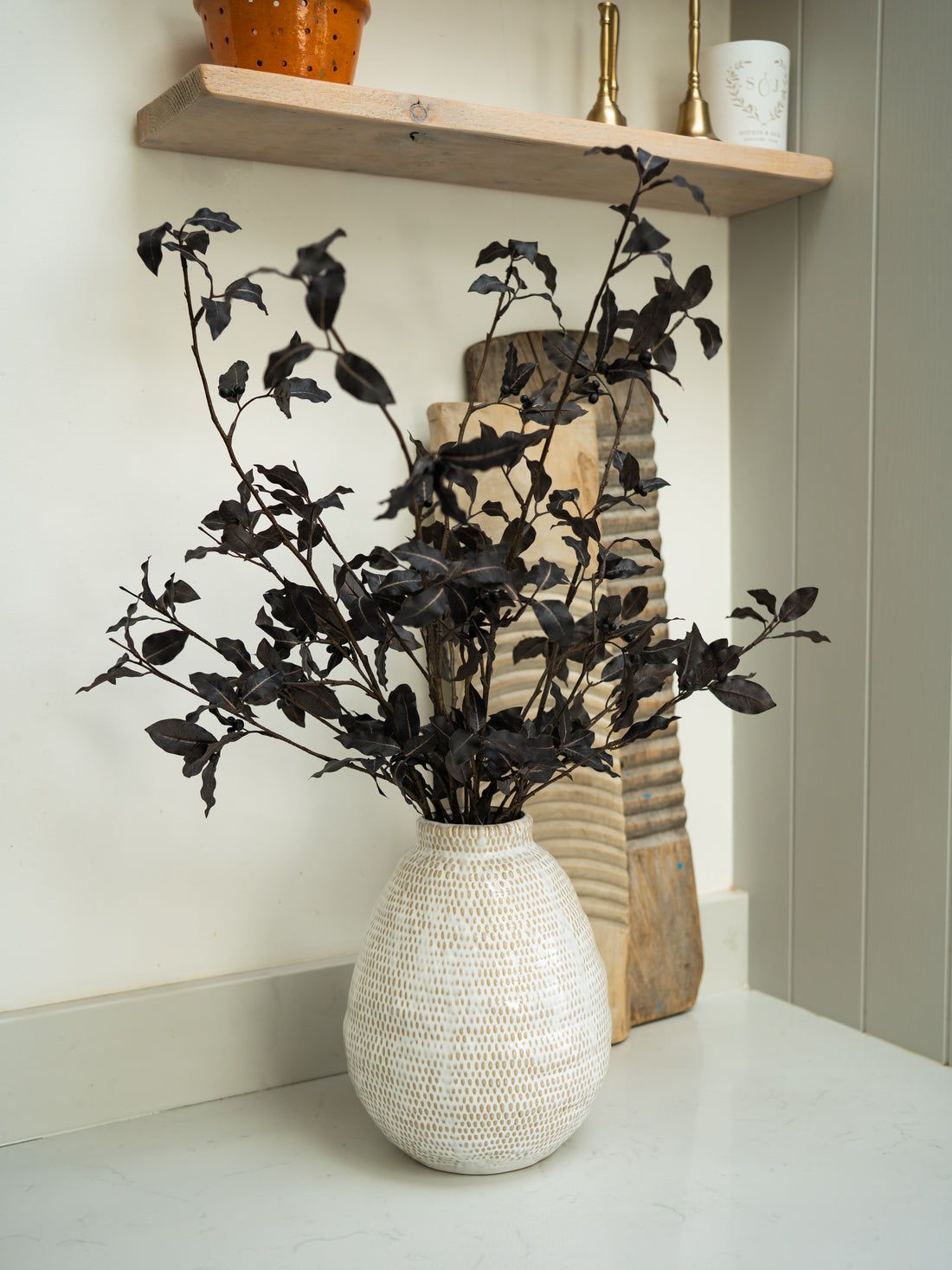 Decorative vase with Faux Pittosporum Tom Thumb Spray on a shelf against a neutral wall.