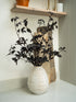 Decorative vase with Faux Pittosporum Tom Thumb Spray on a shelf against a neutral wall.