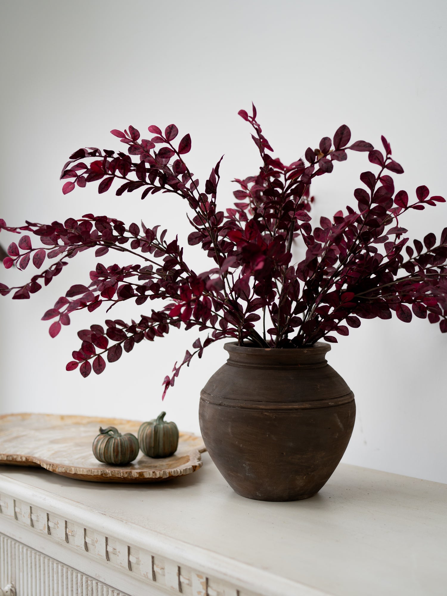 faux dark pink and red small plum leaves styled en masse in rustic brown vase
