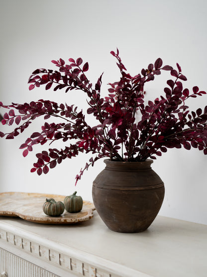 faux dark pink and red small plum leaves styled en masse in rustic brown vase