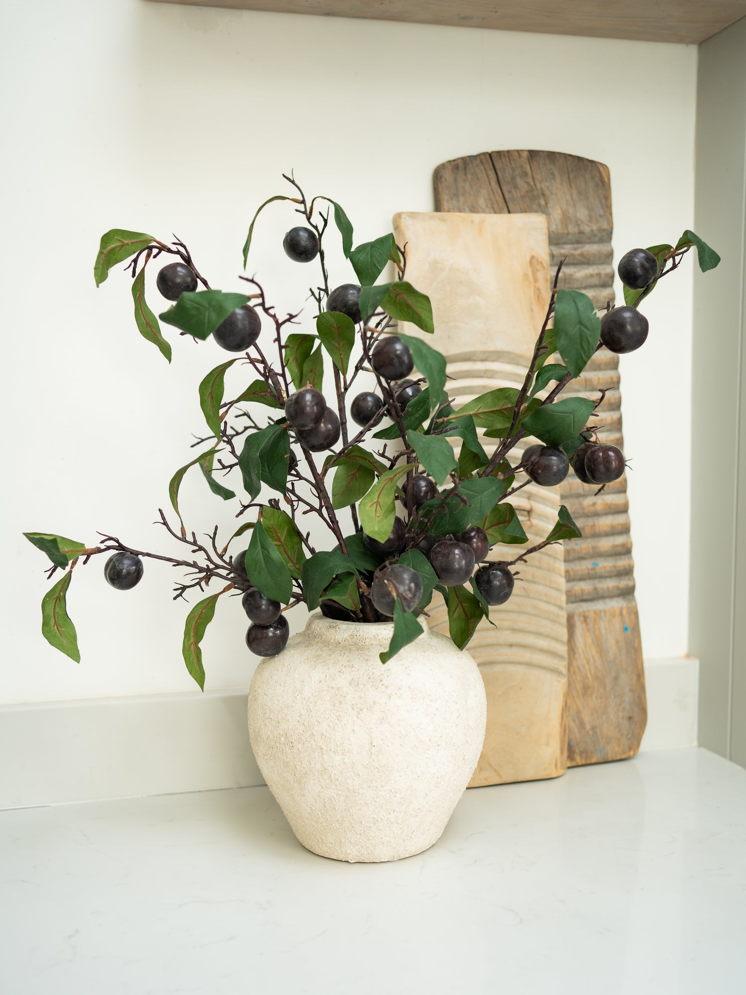 Decorative faux plum leaves stems in rustic textured vase on a shelf