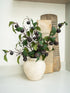 Decorative faux plum leaves stems in rustic textured vase on a shelf