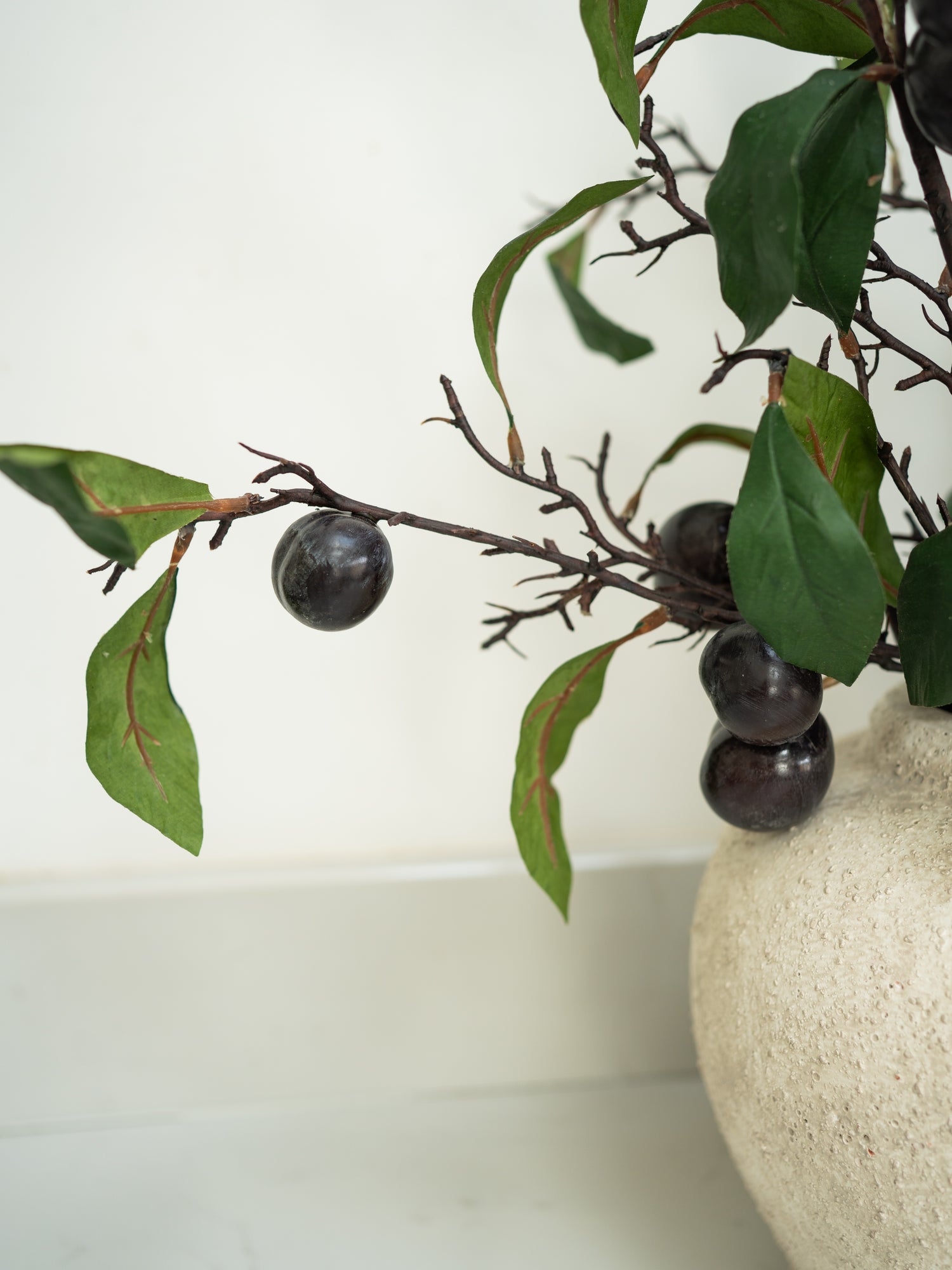 Decorative arrangement with branches and fruits in a textured vase on a white background
