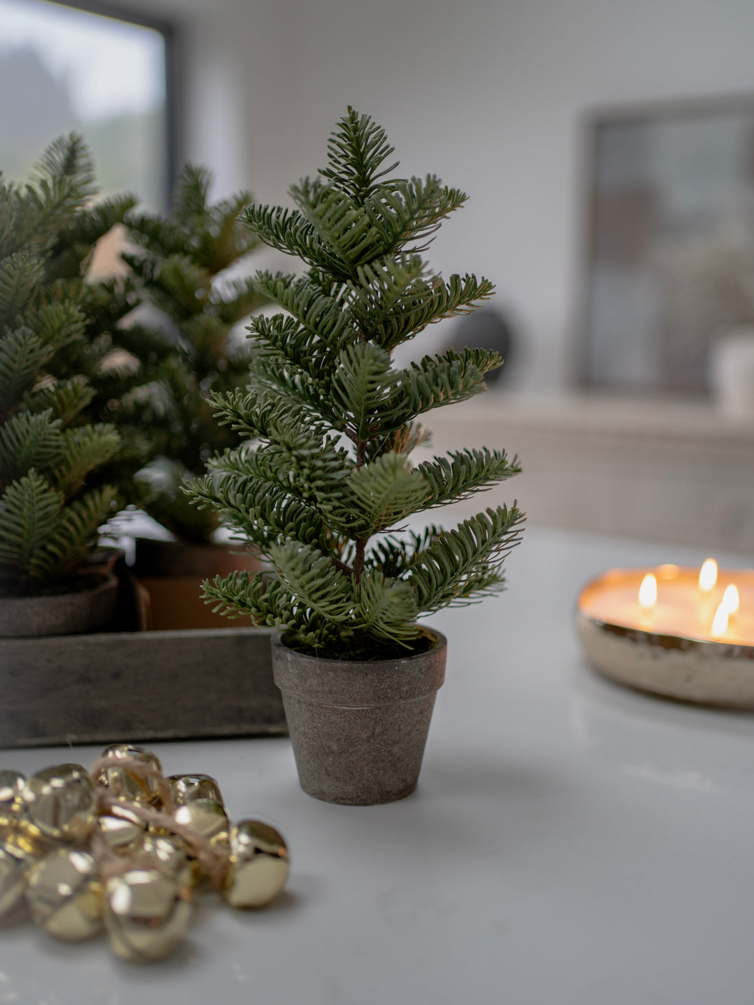 Small potted Christmas tree on a table with gold ornaments and a candle in the background.