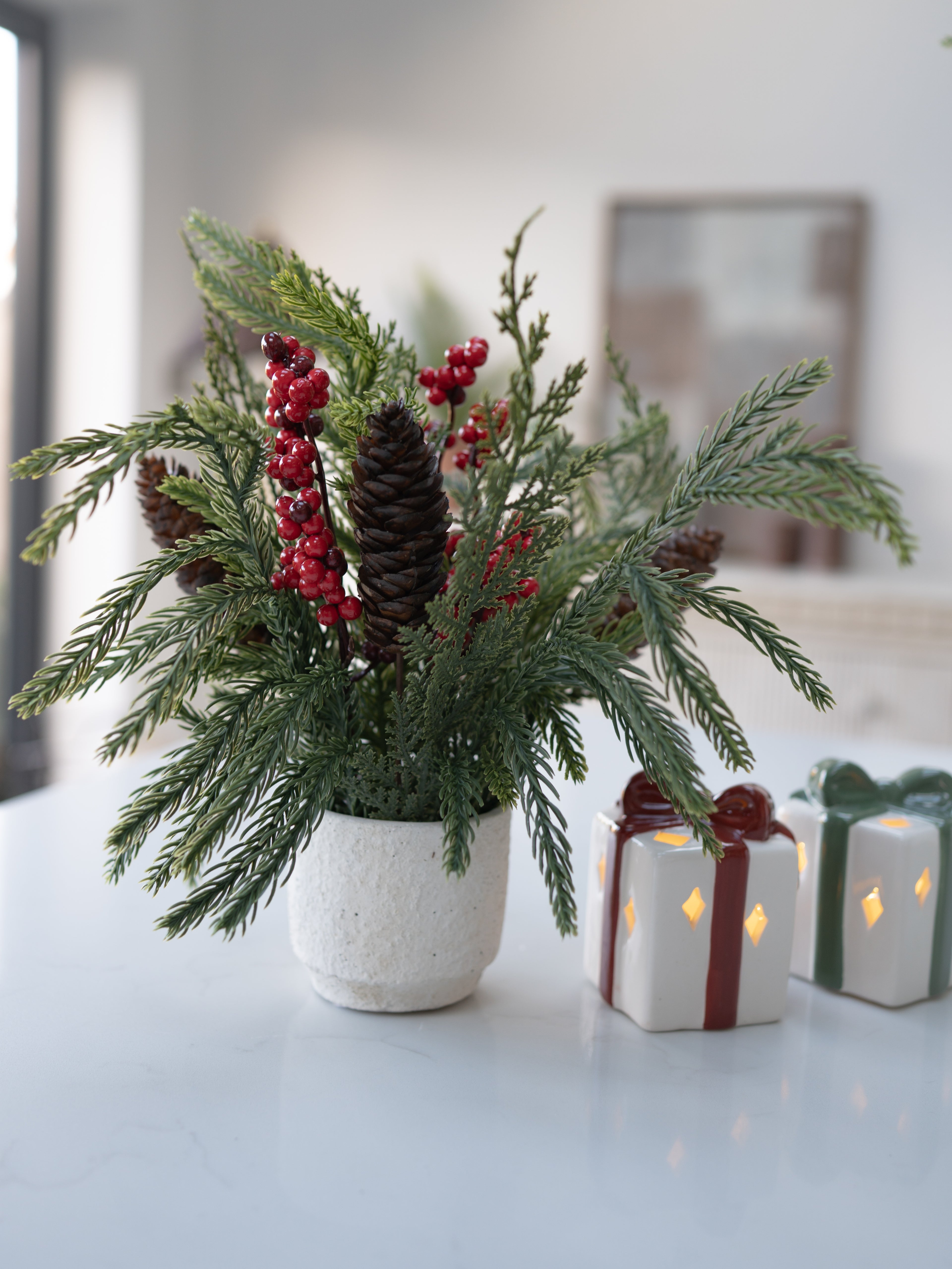 Decorative arrangement with greenery, red berries, and pinecones on a white surface.