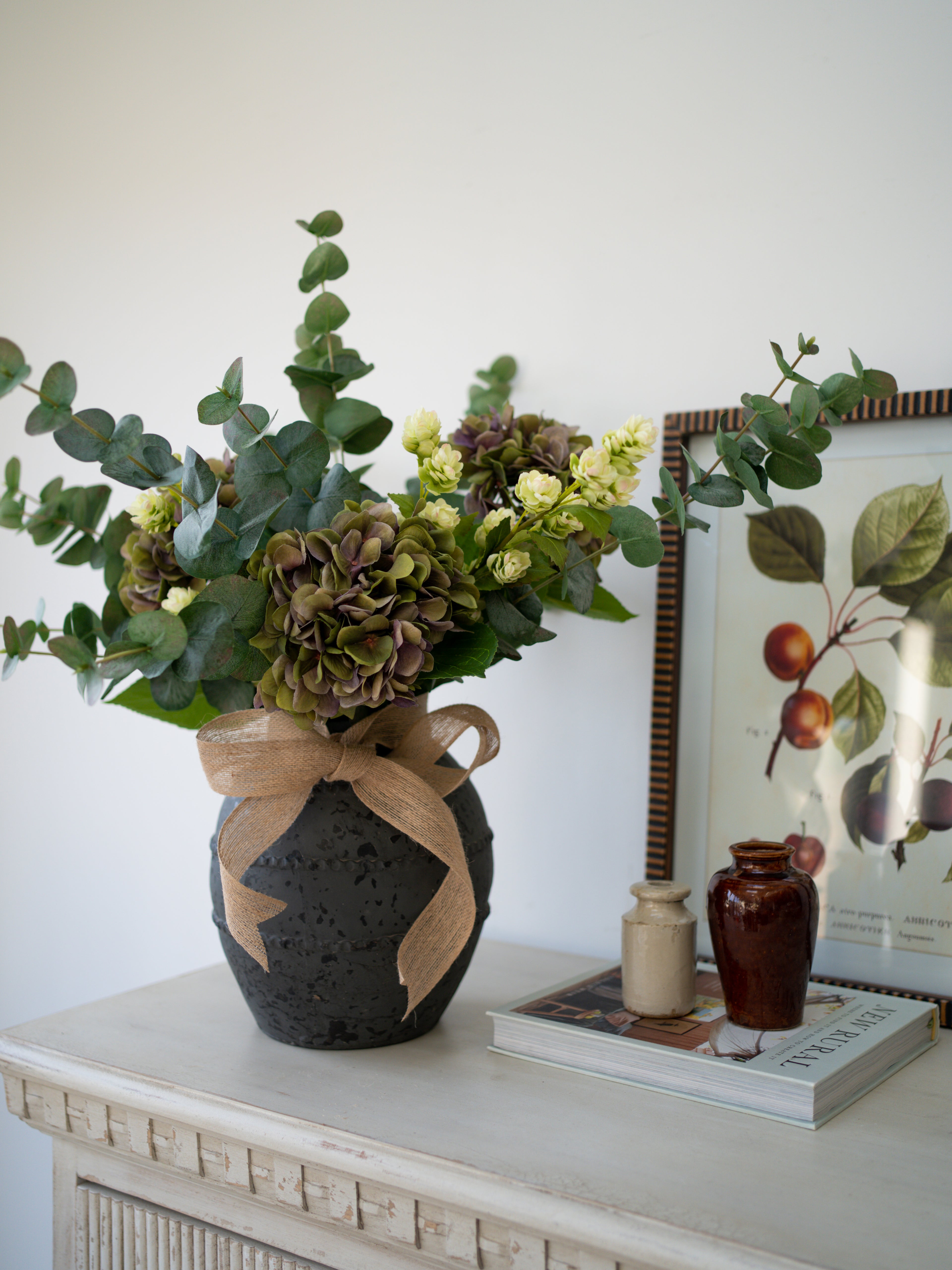 Faux Purple Hydrangea, Hops and Eucalyptus Floral Arrangement in black cement ridged vase with hessian bow