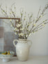 White vase with branches and blossom flowers on a neutral background