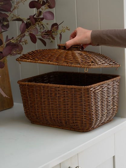 Wicker storage basket with a lid on a white surface, held by a hand.