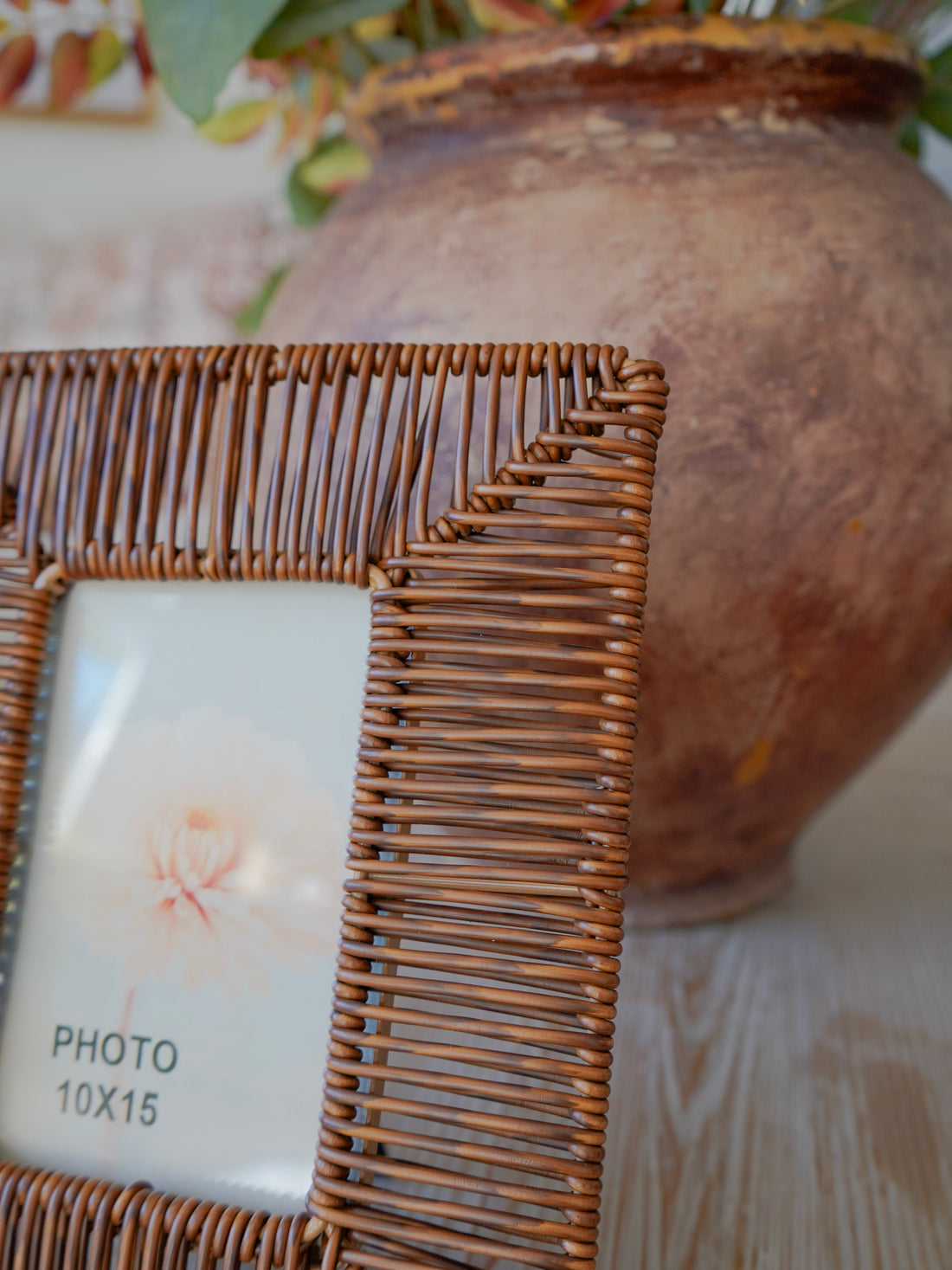 Wicker photo frame with a white card inside, next to a textured brown vase.