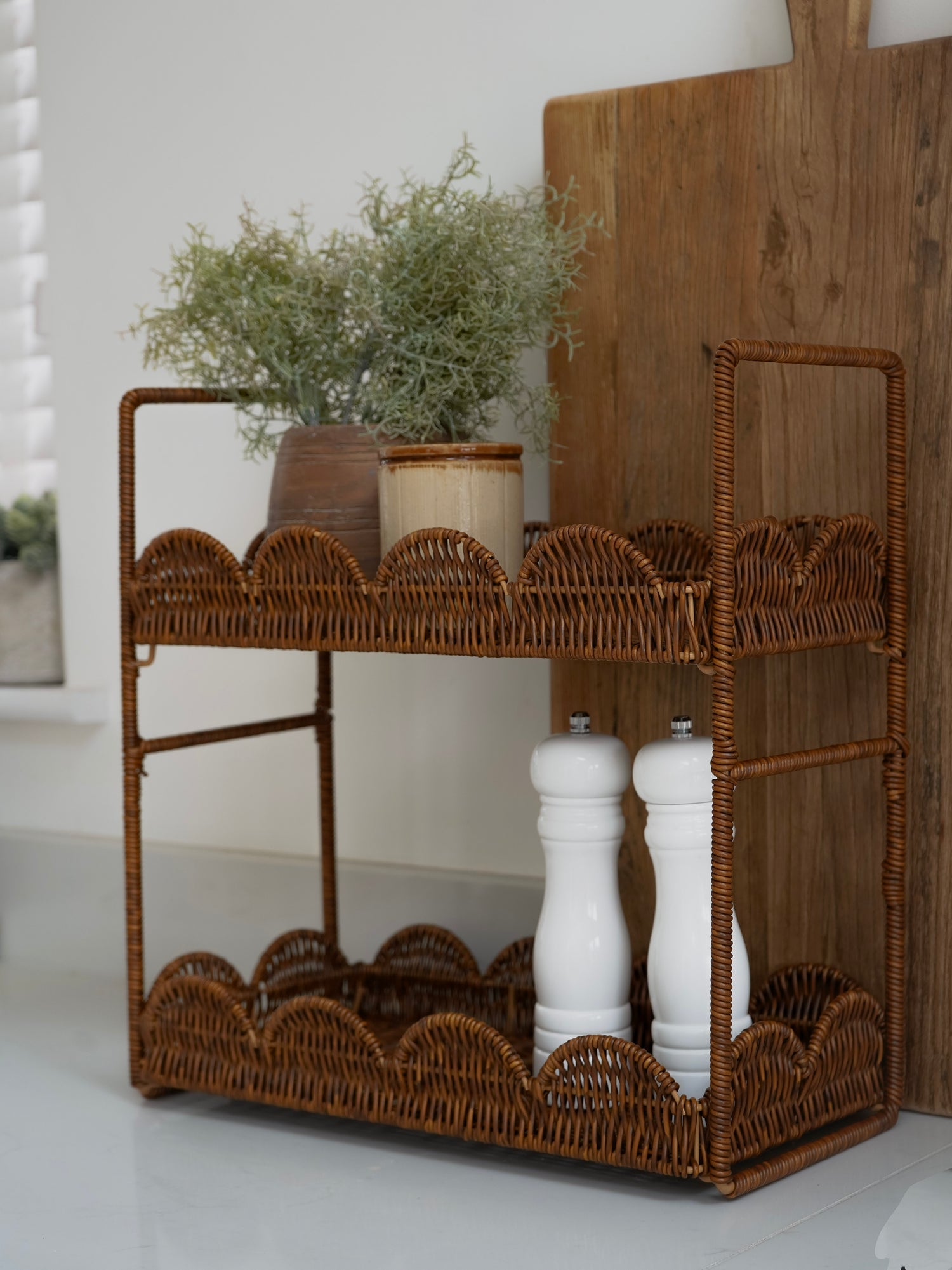Wicker bar cart with shelves, plants, and salt and pepper shakers on a white surface.