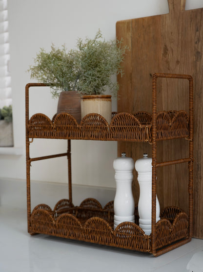 Wicker bar cart with shelves, plants, and salt and pepper shakers on a white surface.