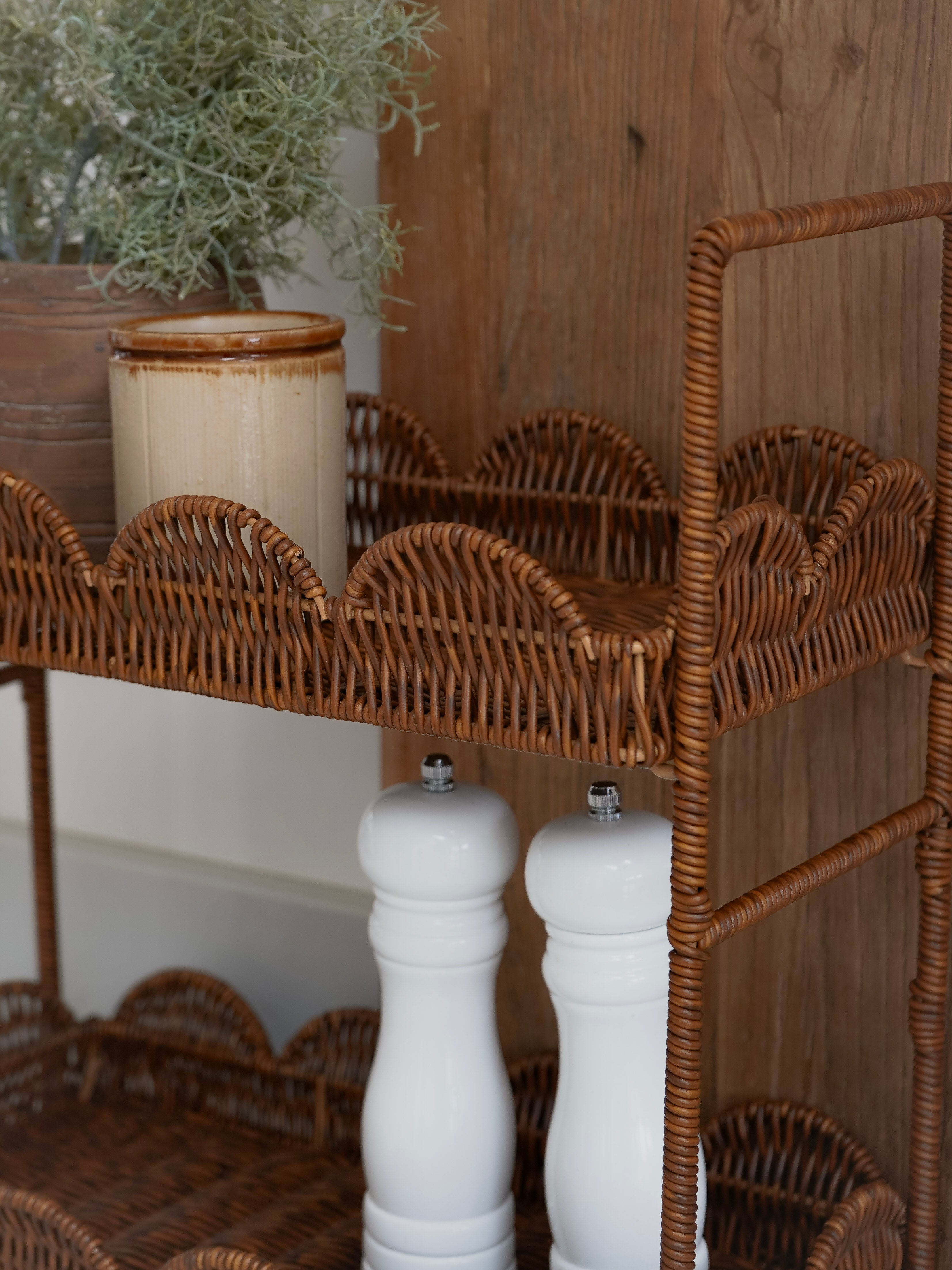 Wicker shelf with white salt and pepper shakers against a wooden wall.