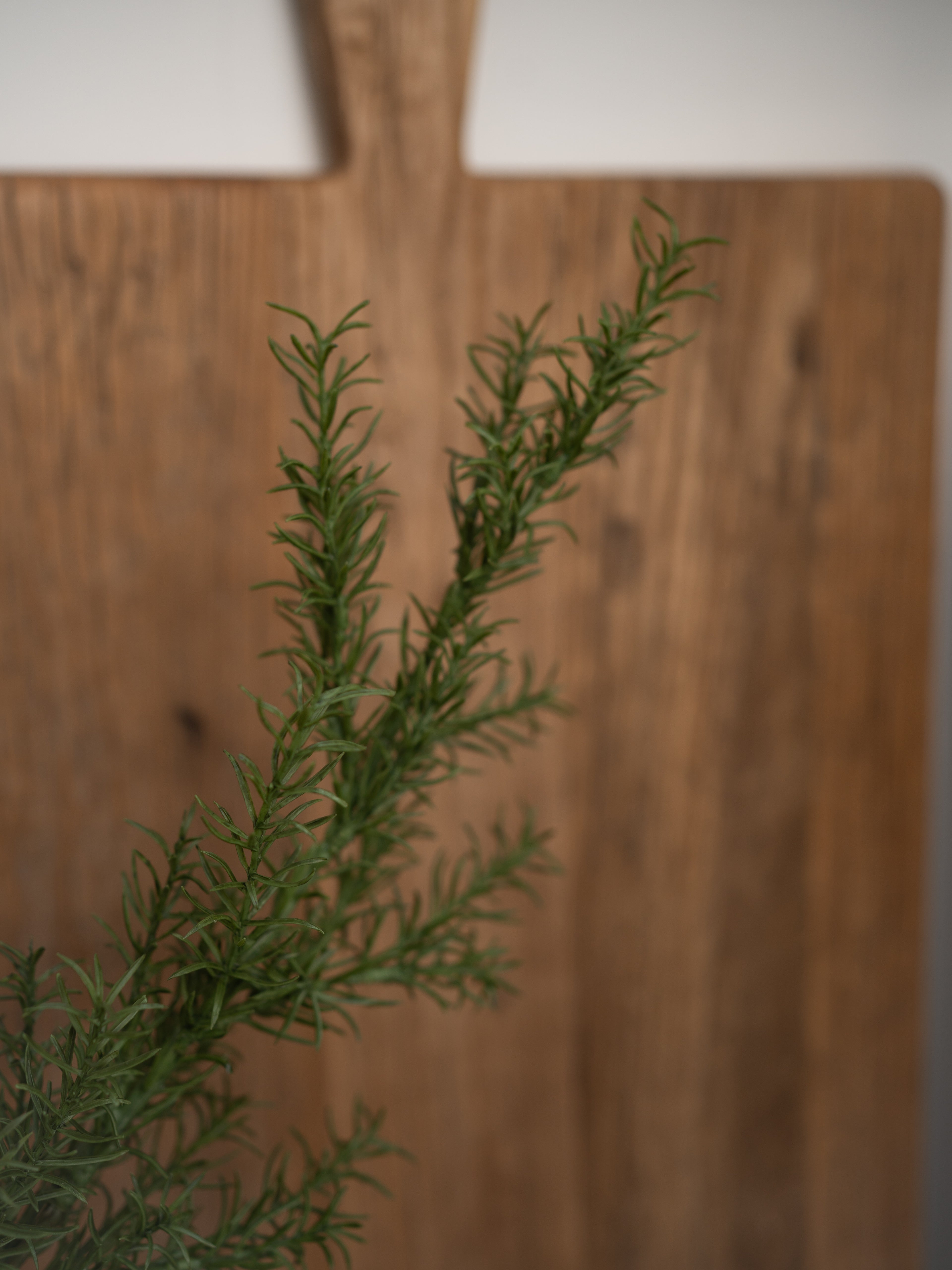 faux rosemary herb on a wooden cutting board with a blurred background