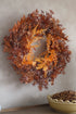 Autumn wreath with leaves and pinecones on a neutral wall.