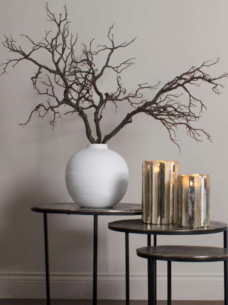 White vase with branches on a table against a plain wall