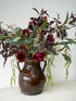 Brown ceramic vase with whimsical red flowers and green leaves on a white surface