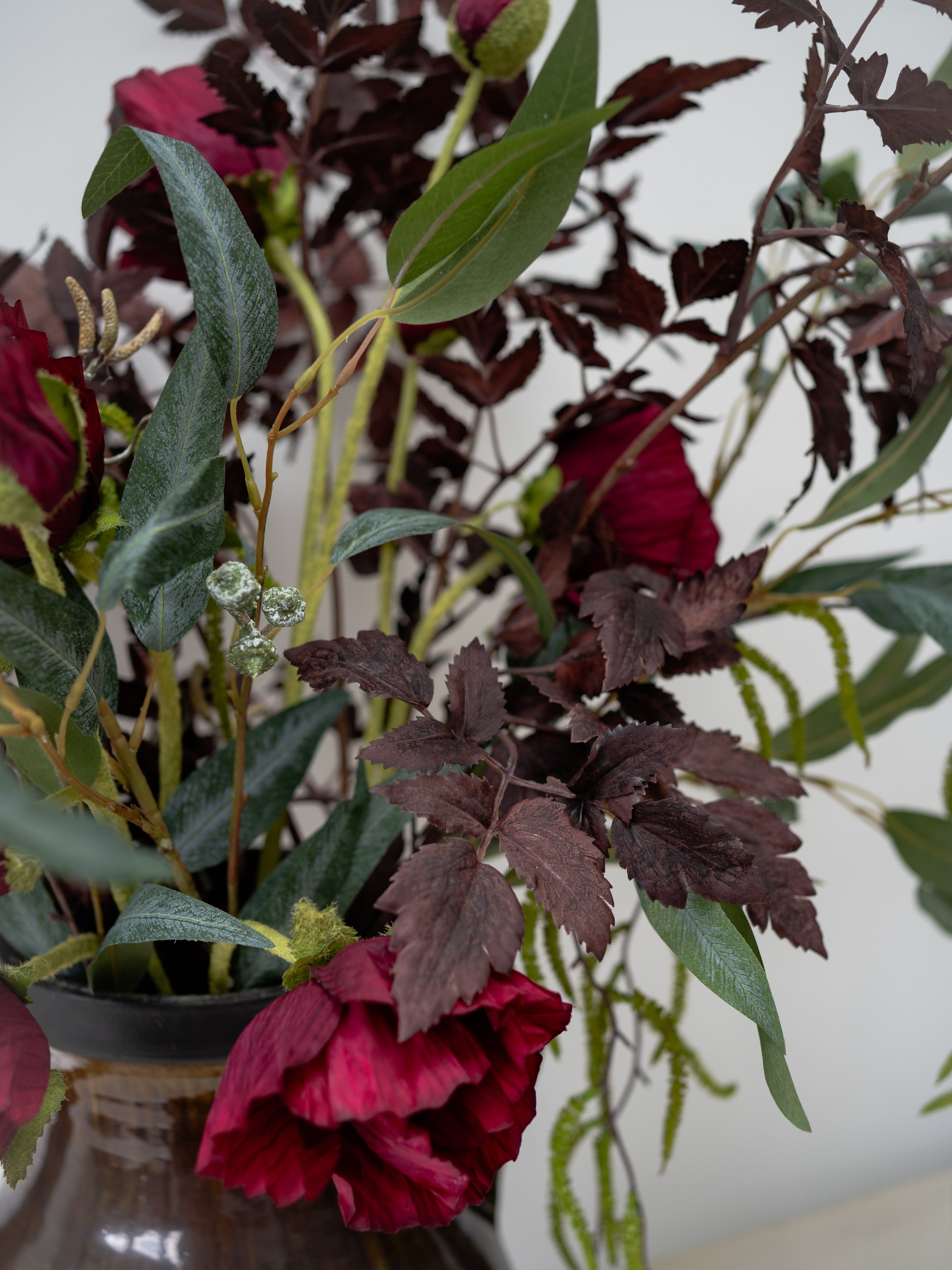 Artificial faux floral arrangement with red and green leaves in a vase against a white background