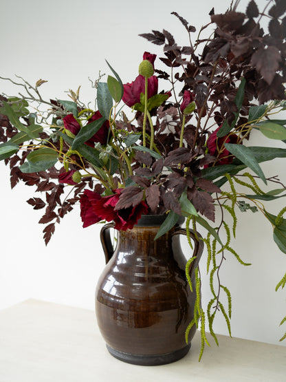 Floral arrangement in a brown vase on a white surface with a white background
