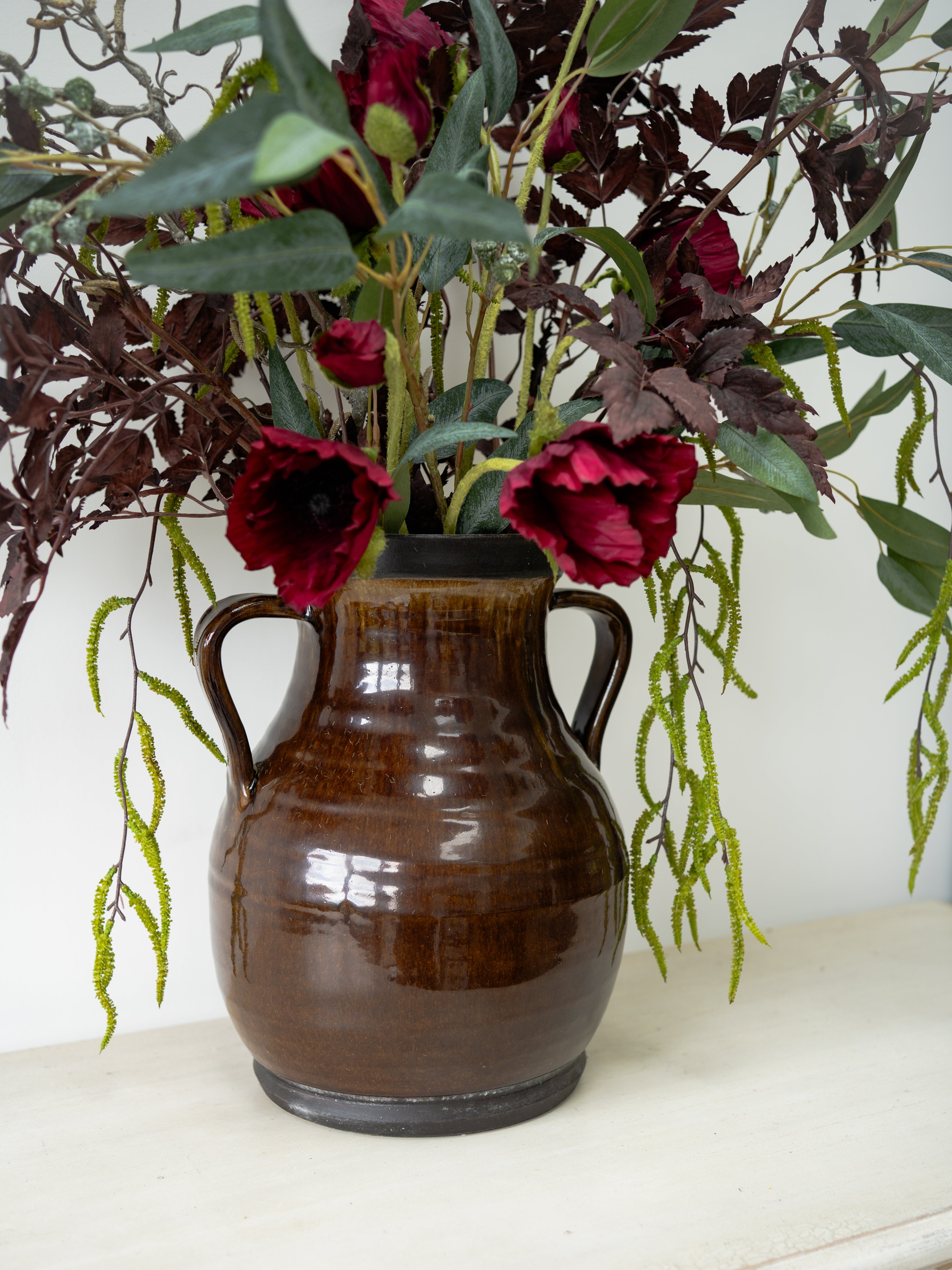 Brown ceramic vase with red flowers on a white surface