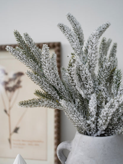 Frosted artificial plants in a white vase against a neutral background
