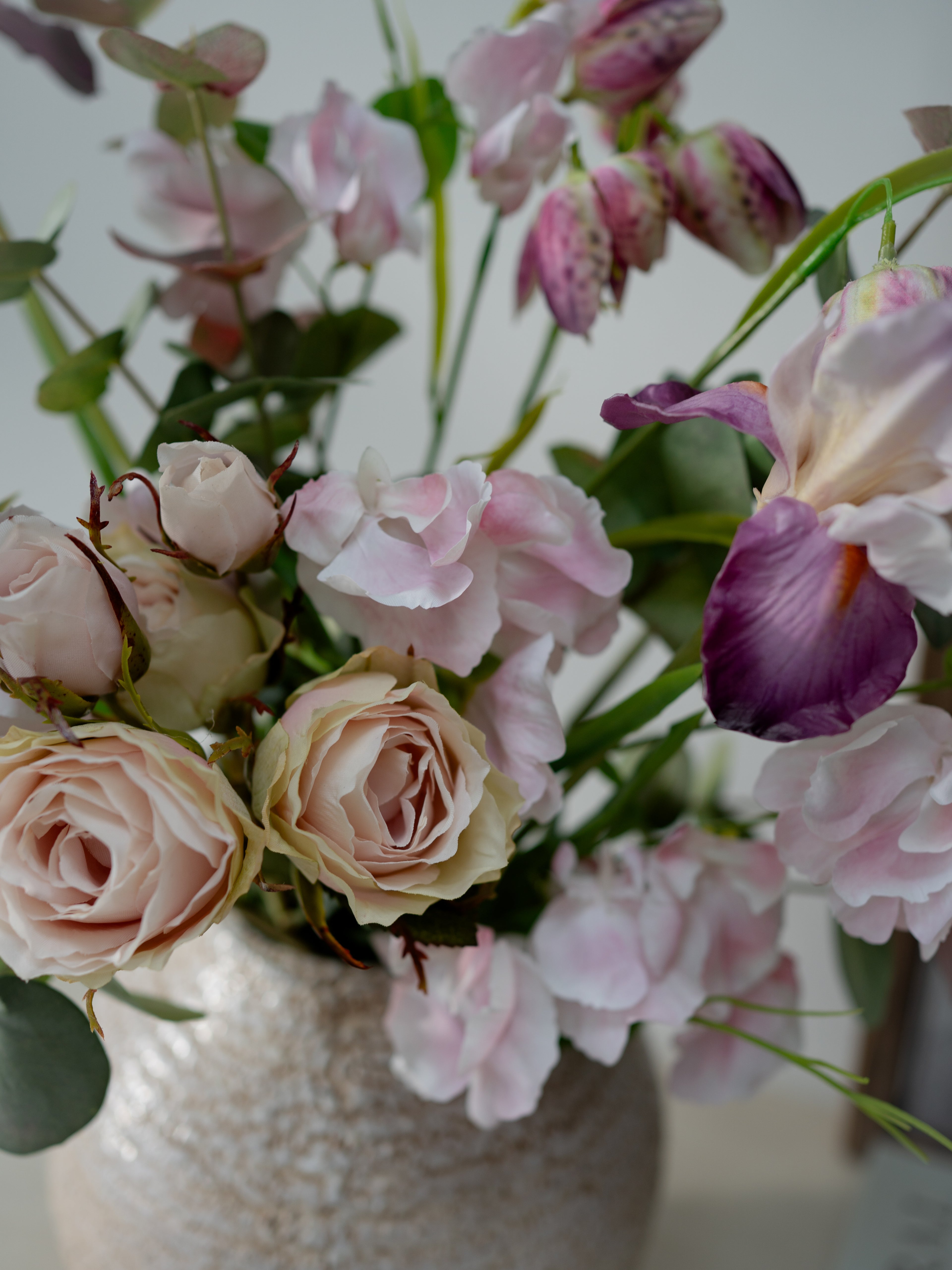 Bouquet of faux pink and purple flowers in a textured vase against a neutral background