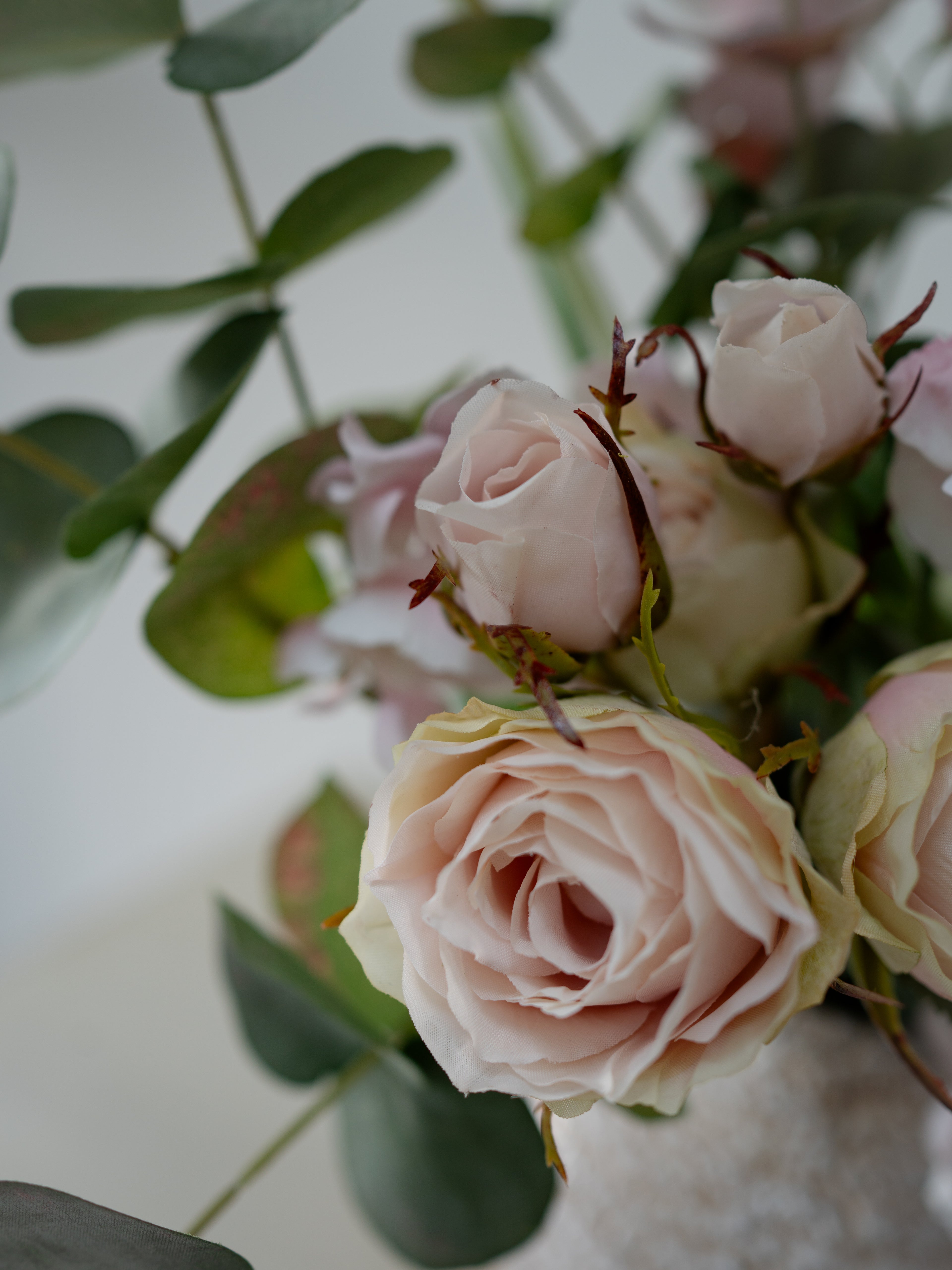 Close-up of artificial pink roses with green leaves on a light background
