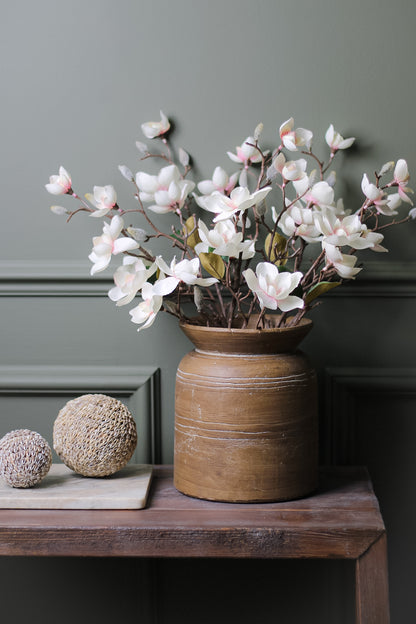 Faux Soft Pink Magnolia Stems in brown rustic vase on wooden table with decorative shell spheres