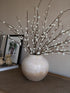 Decorative vase with Faux Soft White Pussy Willow branches on a textured surface