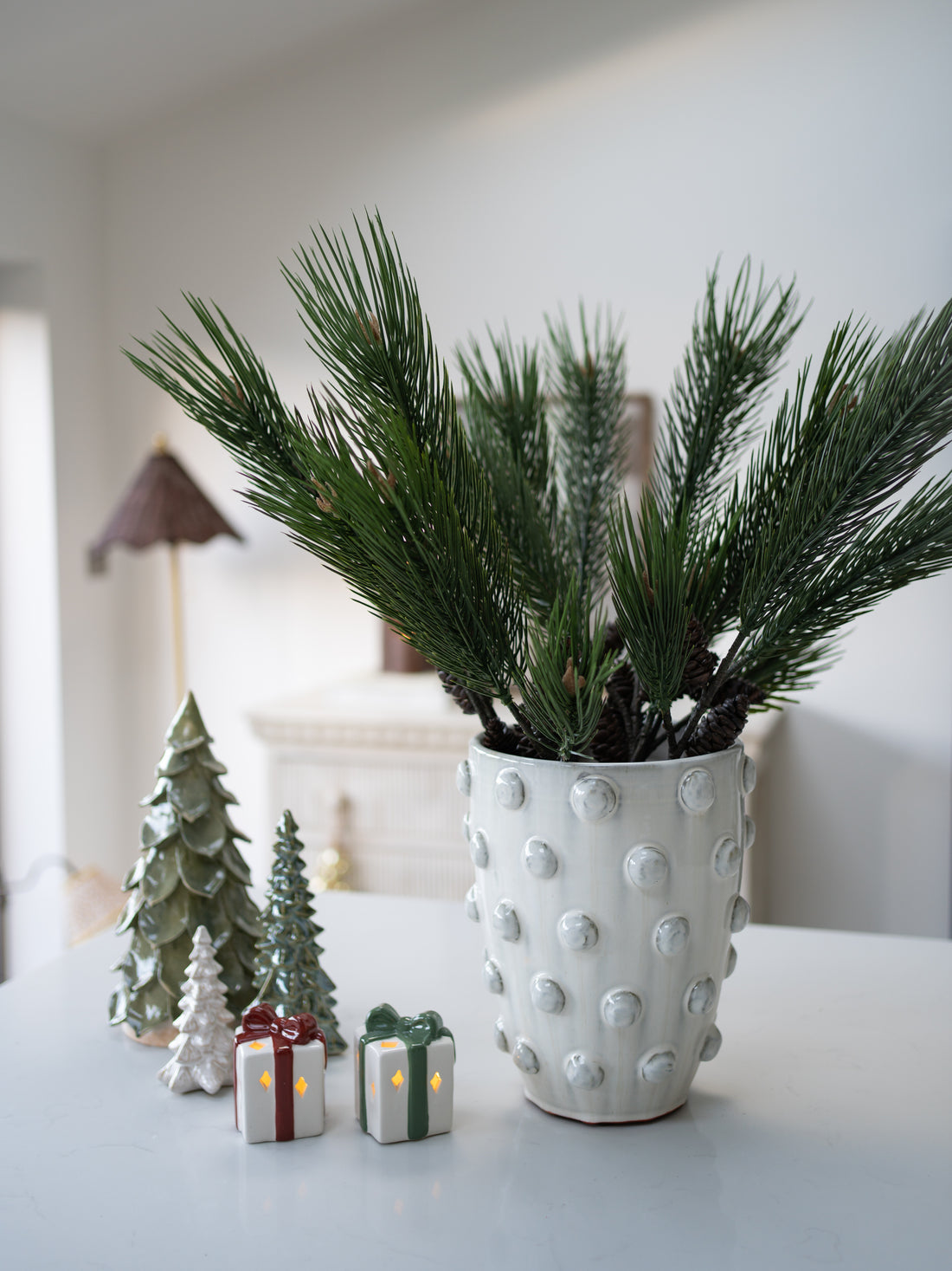 Decorative faux tall pine branch with small Christmas-themed figurines on a table.
