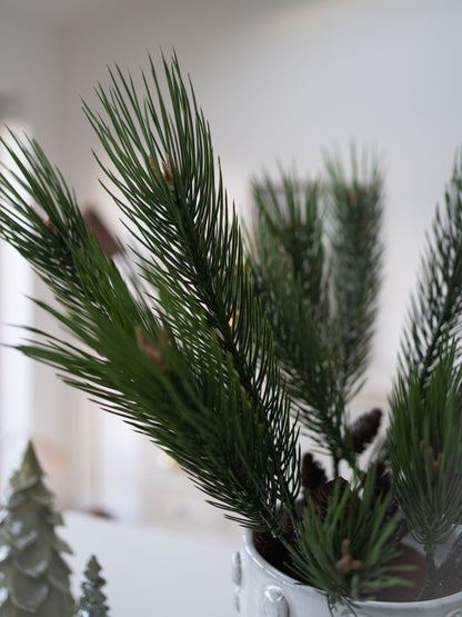 Artificial pine tree branches with cones in a pot on a blurred background
