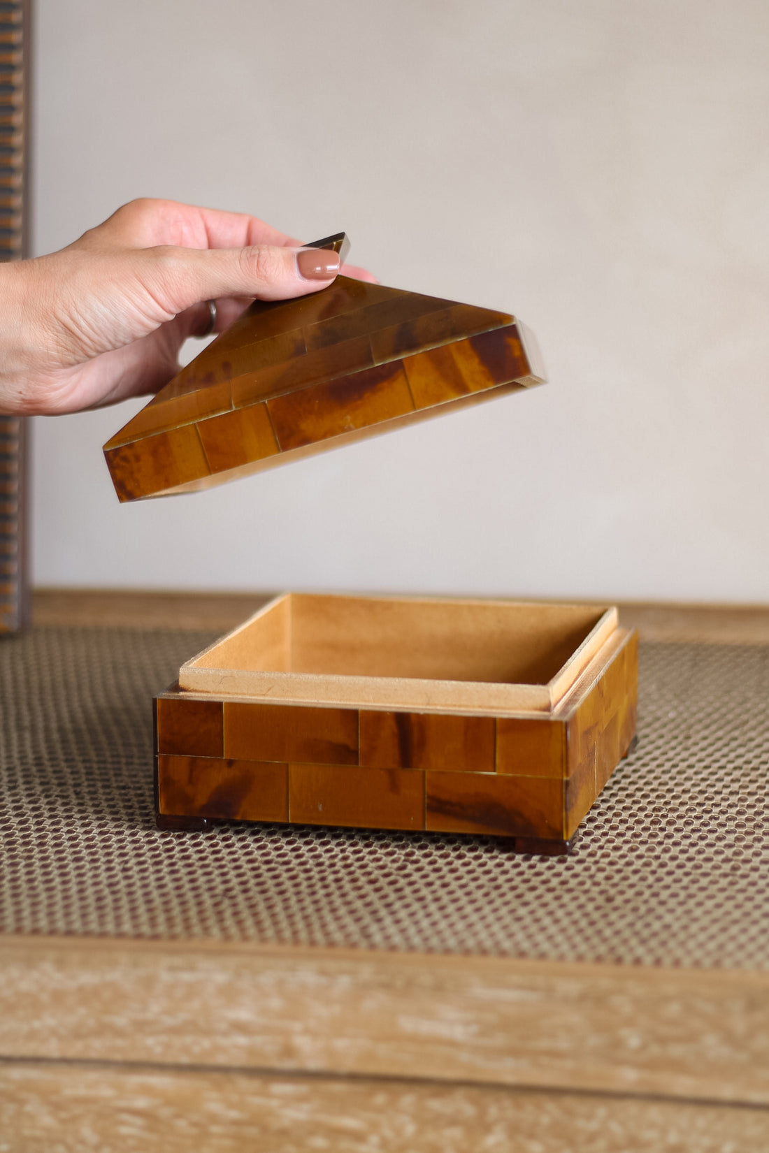 Wooden box with a lid being held open by a hand on a wooden surface.