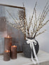 Decorative arrangement with a vase of branches, candles, and a framed picture on a surface.