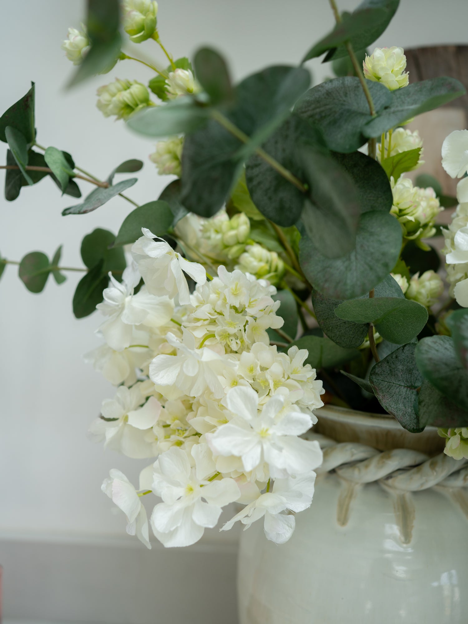 White flowers and green leaves in a woven vase against a light background