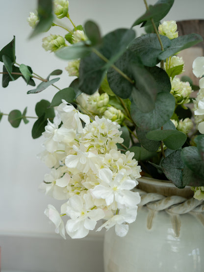 White flowers and green leaves in a woven vase against a light background