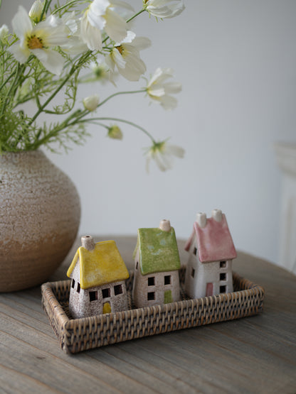 pastel toned roof stoneware houses on grey washed rattan tray with white faux cosmos and vase in the background on grey wooden table