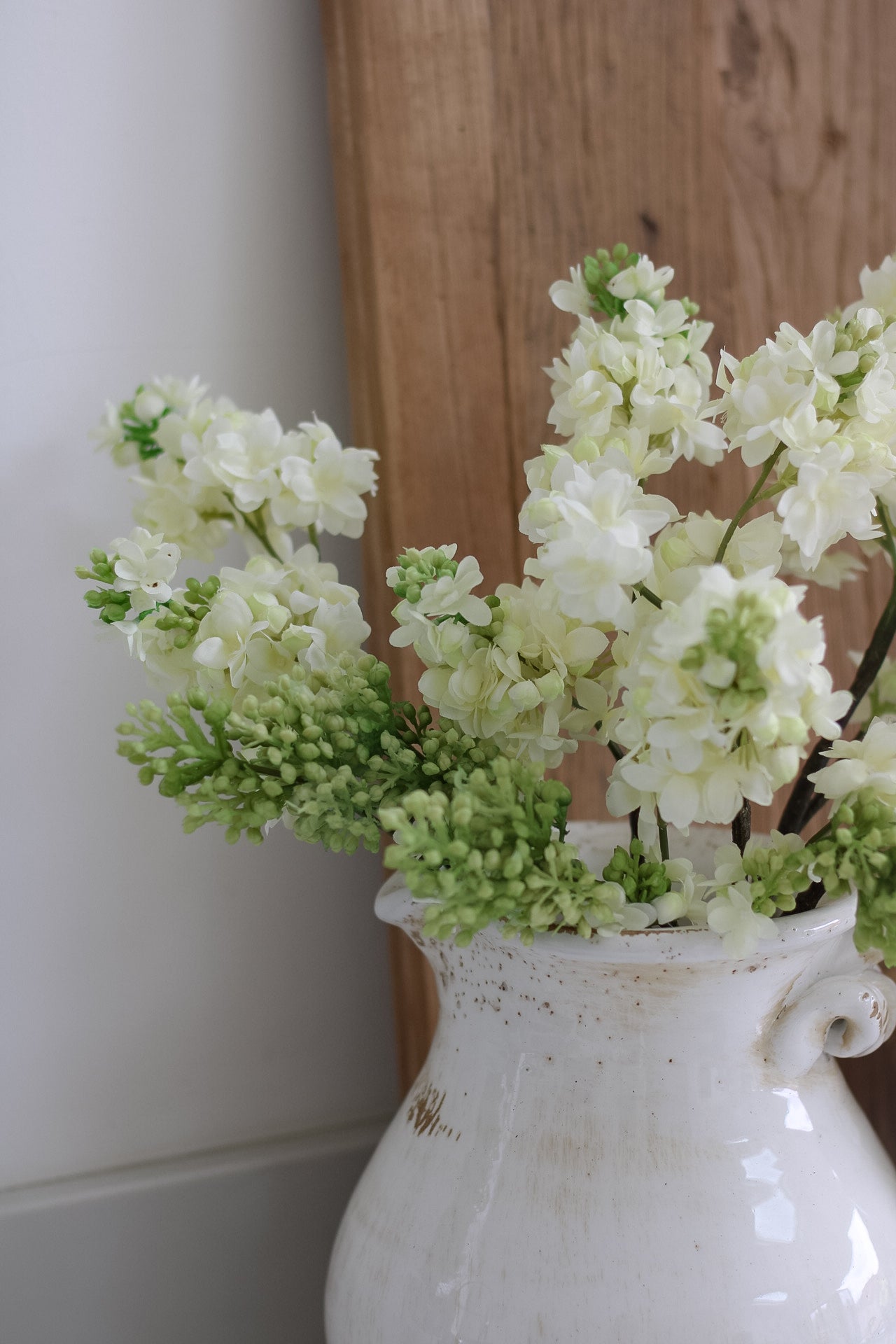 White vase with green and white flowers against a wooden background