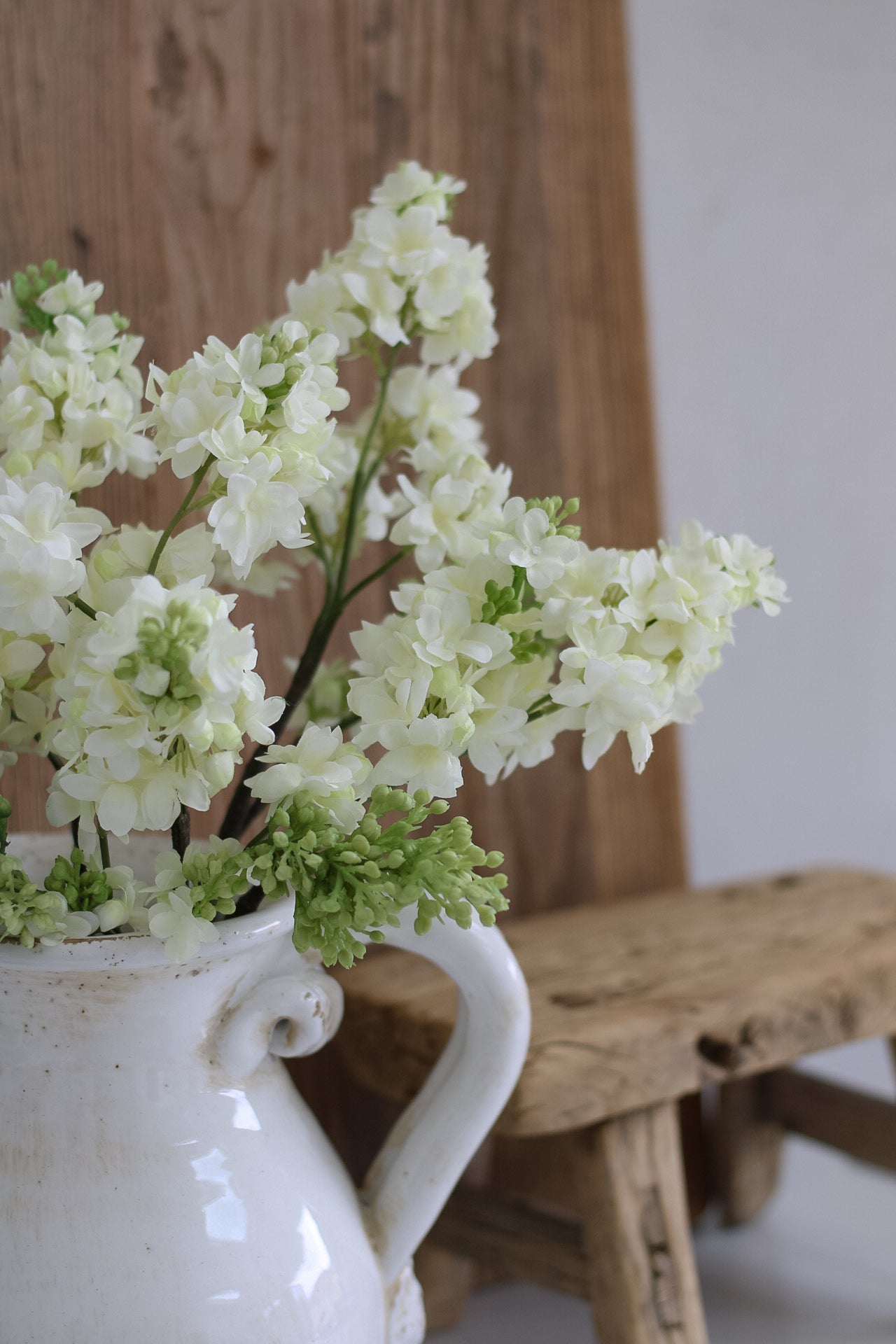 White vase with white flowers and green leaves against a wooden background