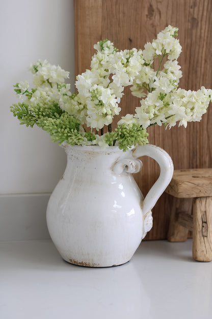 White ceramic pitcher with white flowers on a light surface with wooden background
