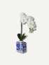 Faux white orchid in a blue and white decorative vase on a light gray background