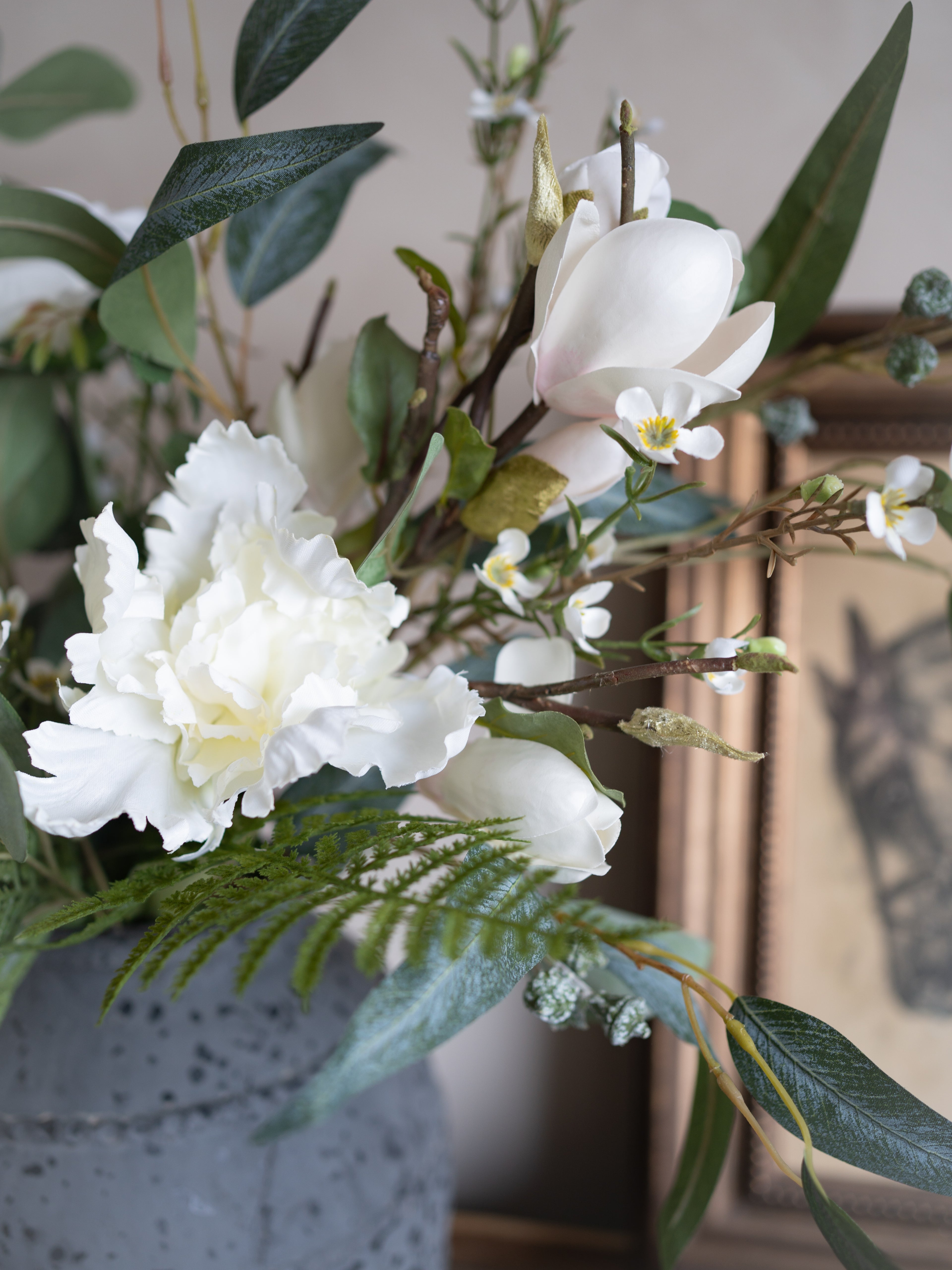 Artificial flower arrangement with white flowers and green leaves in a gray pot.