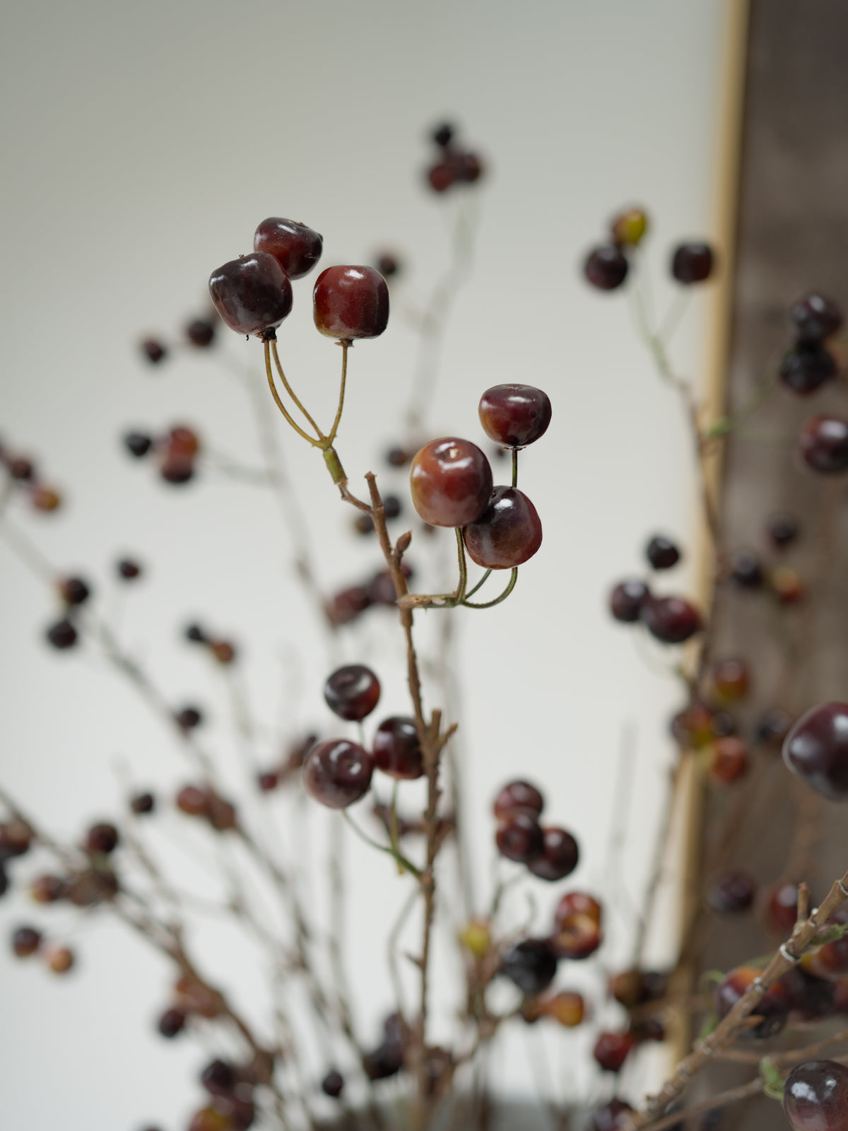 Artificial wild cherries on thin brown branches, arranged against a soft-focus neutral background.