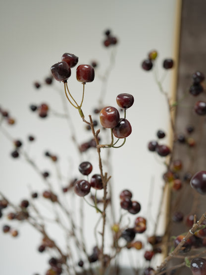 Artificial wild cherries on thin brown branches, arranged against a soft-focus neutral background.
